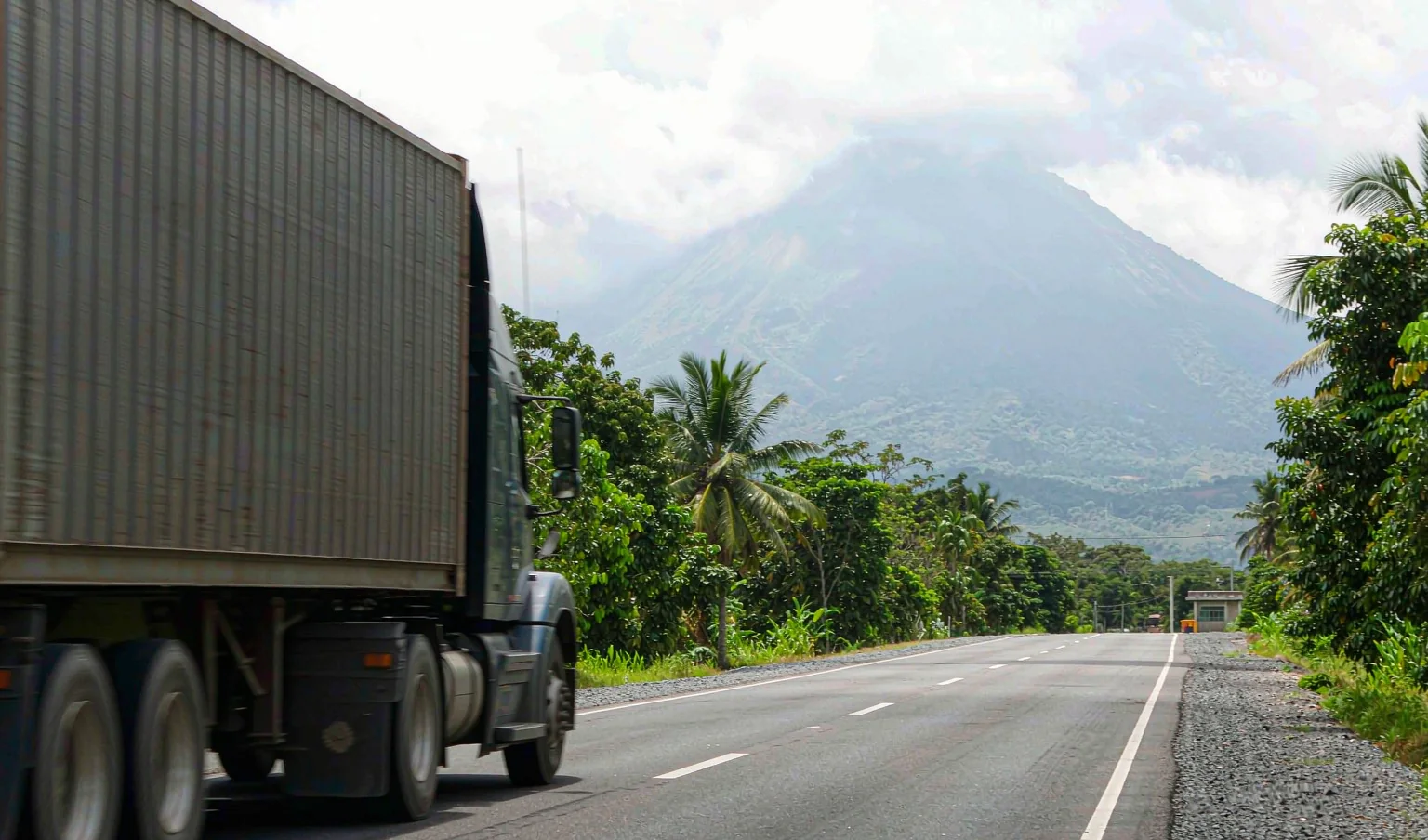 Semi truck hauling a container on a tropical highway toward volcanic highlands - inland delivery from Acajutla to San Salvador by CargoSolid