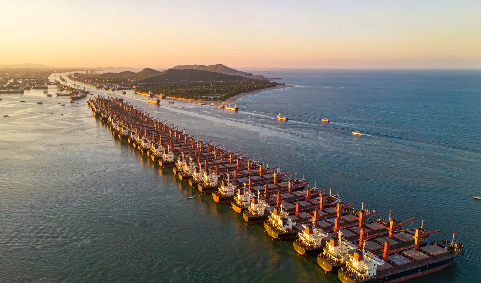 Cargo ships anchored in a queue waiting at a canal entrance at sunset - Panama Canal transit delays by CargoSolid